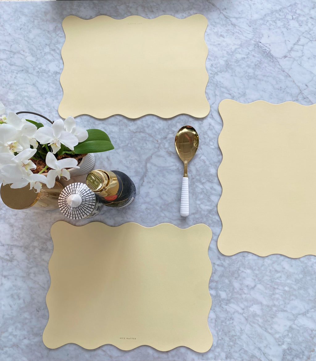 Beige scalloped placemats on a marble table with silverware and a vase of flowers.